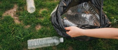 Kapalı el, parkta çöp plastiği topluyor. Çimlerin üzerinde plastik şişe temizleyen bir gönüllü. Çevre, geri dönüşüm ve koruma kavramı.