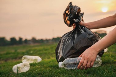 Kapalı el, parkta çöp plastiği topluyor. Çimlerin üzerinde plastik şişe temizleyen bir gönüllü. Çevre, geri dönüşüm ve koruma kavramı.