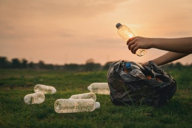 Kapalı el, parkta çöp plastiği topluyor. Çimlerin üzerinde plastik şişe temizleyen bir gönüllü. Çevre, geri dönüşüm ve koruma kavramı.