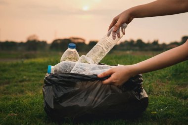 Kapalı el, parkta çöp plastiği topluyor. Çimlerin üzerinde plastik şişe temizleyen bir gönüllü. Çevre, geri dönüşüm ve koruma kavramı.