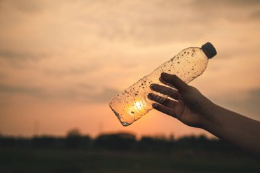 Kapalı el, parkta plastik şişe topluyor. Çöpleri temizleyen bir gönüllü. Çevre, geri dönüşüm ve koruma kavramı.