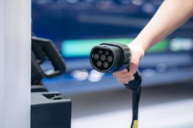 Close Up EV charging at station. Eco and clean energy concept. Hand of Woman Charging Electric Vehicle. Convenient EV Charger in Hand.	