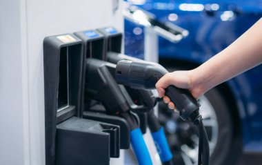 Close Up EV charging at station. Eco and clean energy concept. Hand of Woman Charging Electric Vehicle. Convenient EV Charger in Hand.	