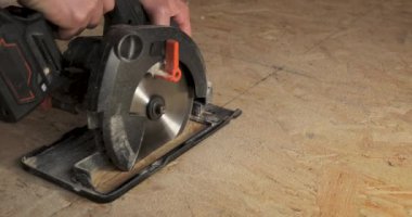 Kontrplak kesmek için testere kullanan bir işçinin yakın çekimi. Çerçeve teknolojisi kullanılarak yeni bir ahşap ev inşa ediliyor..