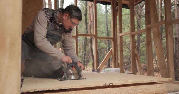 労働者は合板を切るために円形の鋸を使用する フレーム技術を用いた新しい木造住宅の建設 木造住宅建築の概念 — ストック動画