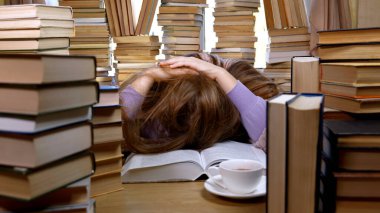 Kütüphanede bir sürü kitap arasında yorgun bir kız. Masada yığınla kitap ve çay var. Okuma ve Eğitim Konsepti.