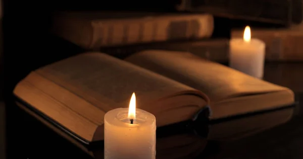 stock image An old book and burning candles. Reading and learning by candlelight at night