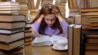 Kütüphanede bir kız kitap okuyor. Masada yığınla kitap ve çay var. Okuma ve Eğitim Konsepti.