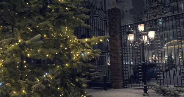 クリスマスツリーを背景にしたクリスマスの夜の豪雪 明るい高いランタンと英語のスタイルで家 — ストック動画