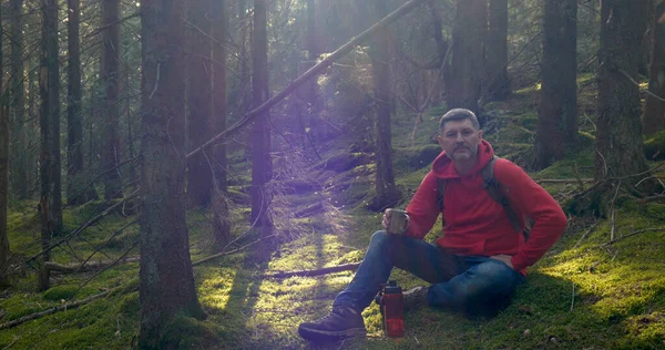 Doğadaki adam. Açık havada seyahat konsepti. Turist su içer ve güzel bir ormanda yosunların üzerinde dinlenir..