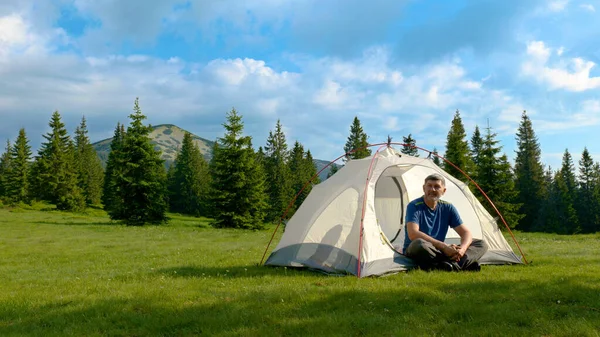 Ormanda kamp ateşi yakınında sakallı bir adam. Kamp dağlardaki güzel bir orman çimenliğinde yer almaktadır. Seyahat kavramı