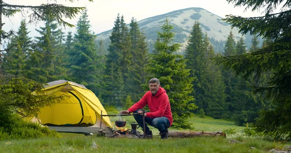 Ormanda kamp ateşi yakınında sakallı bir adam. Kamp dağlardaki güzel bir orman çimenliğinde yer almaktadır. Seyahat kavramı