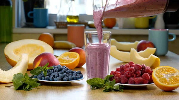 Ahududu Yabanmersinli Meyve Smoothie taze meyve ve meyvelerin arka planında bir bardağa dökülür. Meyve kokteyli yemek için hazır. Sağlıklı ve vejetaryen gıda konsepti