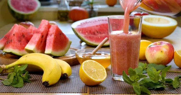 Watermelon banana Smoothie is poured into a glass on the background of fresh fruits. The fruit cocktail is ready to eat. Healthy and vegetarian food concept.