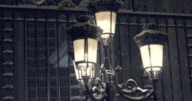 Noel akşamı şiddetli kar yağışı, parlak uzun bir fenerin arka planına ve İngiliz tarzı evlere vuruyor. 4K