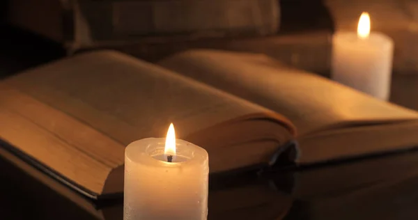 An old book and burning candles. Reading and learning by candlelight at night