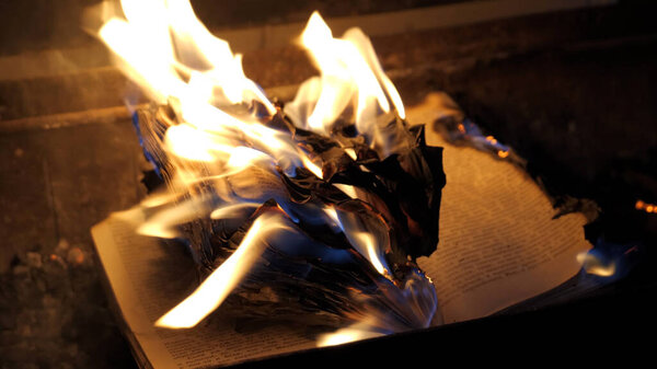 An open book is on fire. Big bright flame, burning paper on old publication in the dark. Book Burning - Censorship Concept