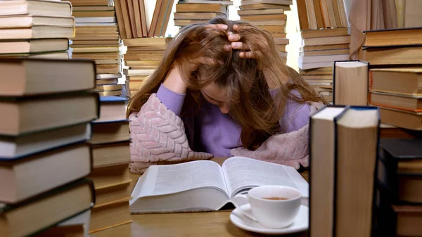 Kütüphanede bir sürü kitap arasında yorgun bir kız. Masada yığınla kitap ve çay var. Okuma ve Eğitim Konsepti.