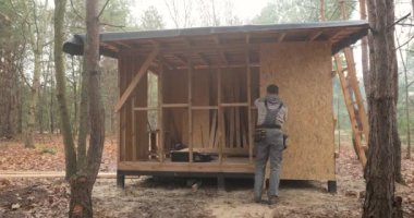 Time lapse of Man worker building wooden frame house. A carpenter mounting wooden OSB panel on the wall of future cottage. Carpentry and construction concept.