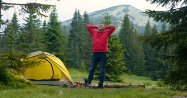 Ormanda kamp ateşi yakınında sakallı bir adam. Kamp dağlardaki güzel bir orman çimenliğinde yer almaktadır. Seyahat kavramı