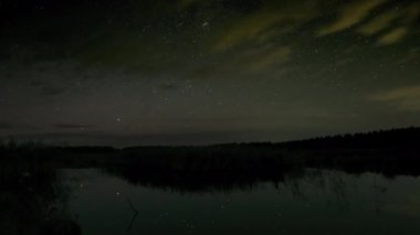 Yıldızların zaman çizelgesi gölün üzerinde gece gökyüzünde hareket ediyor. Efsanevi video 4K