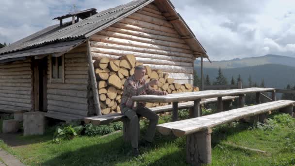 ある男が山の古い木造の家の近くで休んでいる 山中のカルパティアの羊飼いの本当の家 アドベンチャー 街からの脱出の概念 スローモーション映像 — ストック動画