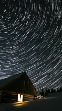 Yıldızların gece gökyüzünde yer değiştirmesi, kışın dağlarda ahşap evler, kutup yıldızının etrafında dönen yıldızlar. dikey görüntüler