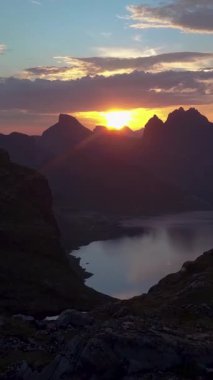 Dağların ve fiyortların üzerinden uçuyor. Güzel gün batımı ve dağlarda dramatik bir gökyüzü. Lofoten Adaları. Norveç, dikey görüntü