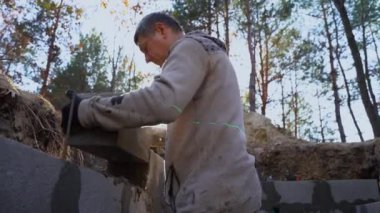 Gerçek bir inşaatçı tuğla döşeyip bodrum duvarı örer.