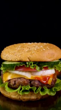 Ateşin arka planında nefis bir burger. Lezzetli burger, taze lahana, soğan, domates ve ızgara biftek. Fast food, ağır çekim, yakın çekim, dikey çekim.