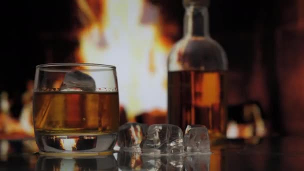 ウイスキー スコッチ バーボンのガラスとボトルは炎で暖炉の背景に対してテーブルの上に立っています アルコールドリンクとホームコンフォートコンセプト — ストック動画