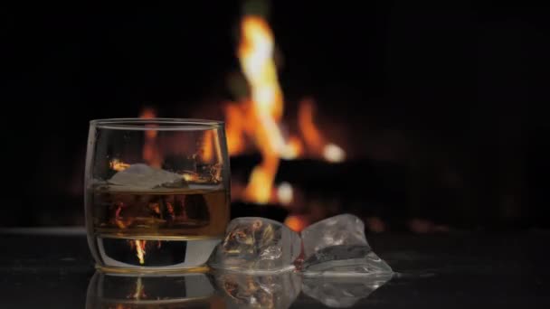 ウイスキー スコッチ バーボンのグラスは 炎のある暖炉の背景に対してテーブルの上に立っています アルコールドリンクとホームコンフォートコンセプト — ストック動画