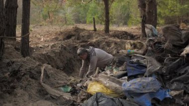 Bir işçi ormanı enkazdan temizler, çöpü bir delikten büyük bir çöp yığınının üzerine atar. Güvenli ekoloji kavramı.