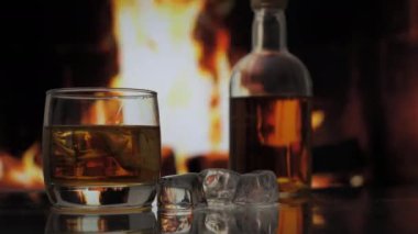 Bir bardak viski, viski, viski ya da viski şöminenin arka planında alevli bir şömine karşısında duruyor. Alkolik içki ve ev konforu.