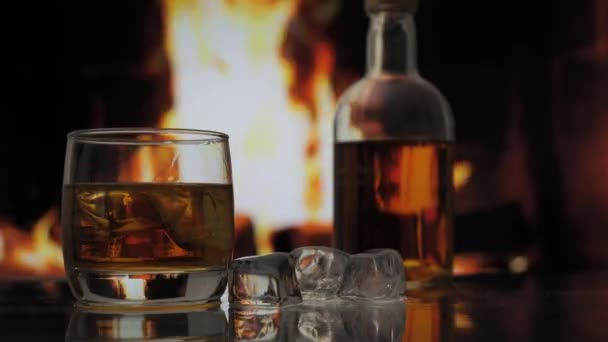 玻璃杯和一瓶威士忌 苏格兰威士忌或波旁威士忌放在有火焰的壁炉前的桌子上 酒精饮料和家庭舒适概念 — 图库视频影像