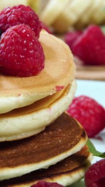 Krep yığınının üzerine bal dökmeye yakın çekim. Lezzetli kahvaltı yemekleri. Krepler ahududu, muz ve nane yaprağı ile servis edilir. Yakın çekim, dikey görüntü