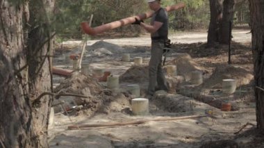 İş kıyafetleri içinde ve güvenlik teçhizatı ile donatılmış bir işçi, kısmen gömülü beton boruların arasına bir orman şantiyesinde büyük yeraltı boruları döşeme sürecinde..