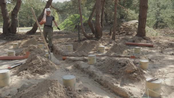 労働者 作業衣装のクラッド 安全ギヤが装備され 森林建設現場に部分的に埋められたコンクリートの基礎の中に大きな地下パイプを敷設する過程にある — ストック動画