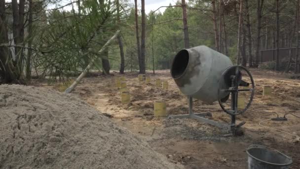 コンクリート製のミキサーは 近くの砂の山を有する森林地帯のクリアリングで動作します 構造プロジェクトの初期段階を示し 地面から突き出したコンクリート製のフットプリント — ストック動画
