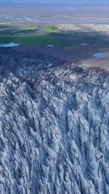 Uçsuz bucaksız bir buzulun, engebeli uçurumlarla çevrili derin mavi çatlakları. Güneş ışığı İzlanda 'daki Svinafellsjokull Buzulu' nun zıt dokularını vurgular. dikey görüntüler