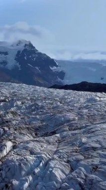 Uçsuz bucaksız bir buzulun, engebeli uçurumlarla çevrili derin mavi çatlakları. Güneş ışığı İzlanda 'daki Svinafellsjokull Buzulu' nun zıt dokularını vurgular. dikey görüntüler