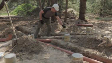 İş kıyafetleri içinde ve güvenlik teçhizatı ile donatılmış bir işçi, kısmen gömülü beton boruların arasına bir orman şantiyesinde büyük yeraltı boruları döşeme sürecinde..