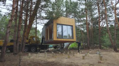 Installation of a Modern Prefabricated Cabin in a Forested Area During. The process involves precise maneuvering and placement of the structure onto a foundation amongst the tall pine trees.