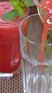 Taze meyvelerin arka planındaki bir bardağa karpuz muzlu meyve suyu dökülüyor. Meyve kokteyli yemek için hazır. Sağlıklı ve vejetaryen gıda konsepti. dikey görüntüler