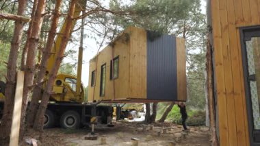 Bir vinç prefabrik bir kulübeyi ağaçlık bir alana yerleştirir. Kulübe ahşaptan yapılmıştır ve modern bir tasarıma sahiptir. Uzak bir yerde küçük, şebeke dışı bir ev inşa etme süreci.