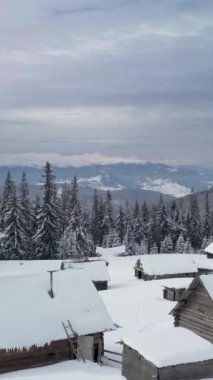 Huzurlu bir dağ manzarasında, karla kaplı çam ağaçları ve rahat kulübelerin sergilendiği sakin bir manzara. Dikey görüntüler