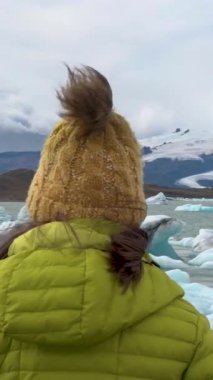 İzlandalı turist, Jokulsarlon Buzul Gölü manzarasının tadını çıkarıyor. Turistlerin uğrak yerindeki açık hava kızı. Vatnajokull Ulusal Parkı, İzlanda. dikey görüntüler