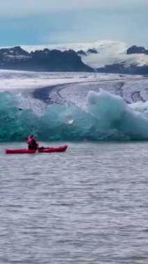 Kayakçı Jokulsarlon, İzlanda 'daki eriyen bir buzul gölünün içinden geçiyor. dikey görüntüler