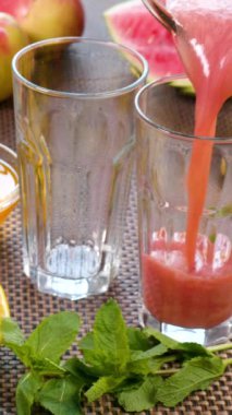 Taze meyvelerin arka planındaki bir bardağa karpuz muzlu meyve suyu dökülüyor. Meyve kokteyli yemek için hazır. Sağlıklı ve vejetaryen gıda konsepti. dikey görüntüler