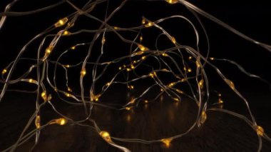 Küçük sarı ampullü bakır tel lambalar ahşap bir yüzeye bağlanır. Işıklar açık ve karanlık arka planı aydınlatıyor..